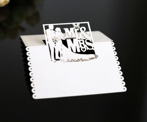 Macro detail of laser-cut white Mr & Mrs wedding place cards on reflective background