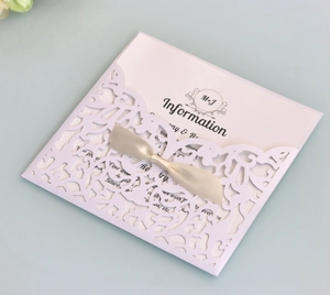 Close-up of laser-cut lavender lace wedding invitation with a cream satin bow and card