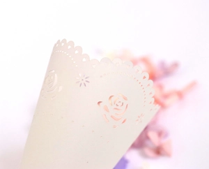 Macro view of laser-cut rose and heart patterns on wedding petal confetti cones