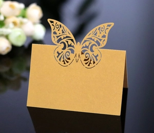 Detailed laser-cut butterfly place card in pearl gold standing on a mirror table