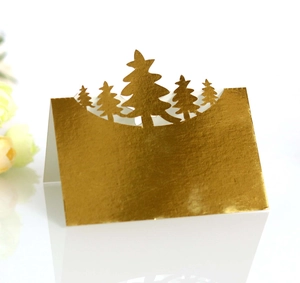 Macro detail of laser-cut gold foil Christmas tree table card on a white mirror surface