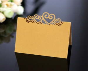 Detail of laser-cut heart pattern on gold wedding place card with reflective surface