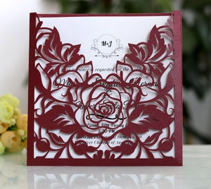 Close-up of laser-cut maroon glitter paper wedding invitation with rose hollow patterns