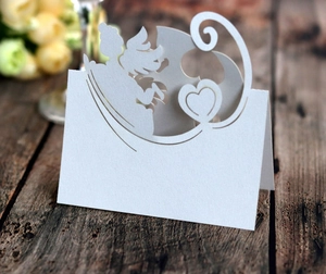 Detailed laser-cut white wedding place card with angel and heart motifs on wood
