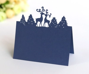 Detailed laser-cut silhouette of reindeer and pine trees on a navy blue place card