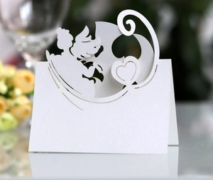 Detailed laser-cut white wedding place card with angel and heart motifs on textured paper