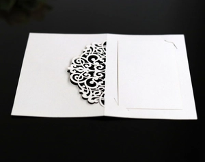 Macro shot of laser-cut white lace wedding place card with elegant European hollow patterns