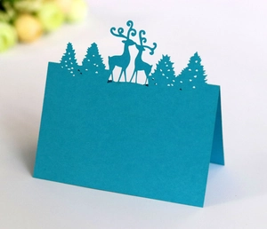Detail of laser-cut bright blue place card with reindeer and pine tree festive design