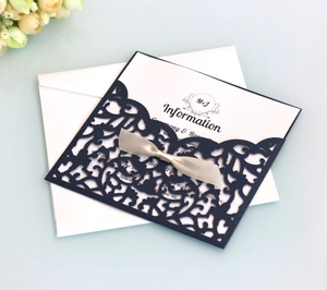 Close-up of navy blue laser-cut lace wedding invitation with silver satin bow and insert