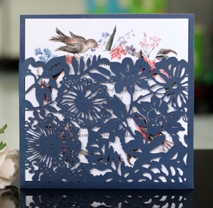 Detail of laser-cut navy floral invitation with colorful bird and flower inner card