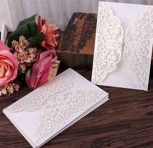Detail of white laser-cut rose wedding invitation covers on a rustic wooden background