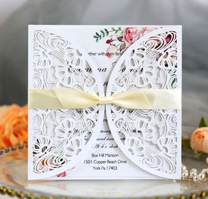 Elegant laser-cut ivory wedding invitation with silk ribbon bow and rose floral insert