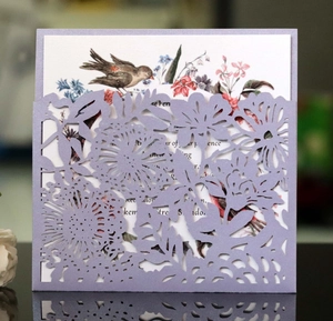 Detail of laser-cut lavender invitation cover with floral watercolor insert card