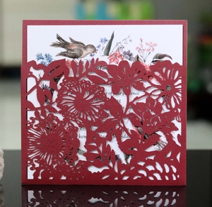Macro detail of laser-cut floral invitation cover in deep red with bird and flower inserts