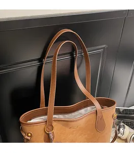 Detail of a brown tote bag featuring long shoulder straps and golden hardware accents