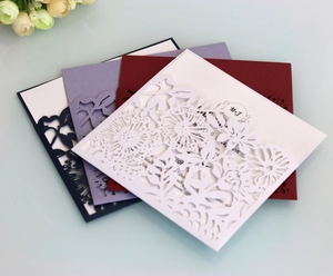 Close-up of laser-cut floral wedding invitations in white, burgundy, purple, and blue