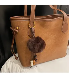 Detail of a brown tote bag featuring golden lettering and a fuzzy brown pom-pom charm