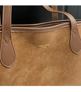 Close-up of caramel brown suede tote bag featuring gold embossed logo and premium stitching