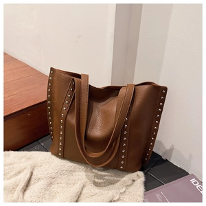 Detailed macro view of the brown pebbled leather surface and silver rivets on the tote bag