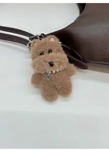 Detail of plush dog bag charm with pearl collar and bone tag on leather tote bag