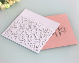 Detail of laser cut floral wedding invitation with white lace sleeve and pink inner card