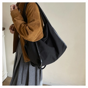 Detail of large black canvas tote bag showing side leather trim and slouchy texture