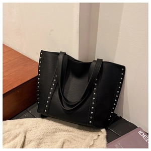 Close-up of black lychee leather tote bag with silver rivet details in a cozy home setting