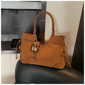 Detail view of a brown suede tote bag featuring a leopard print and pom-pom charm decoration