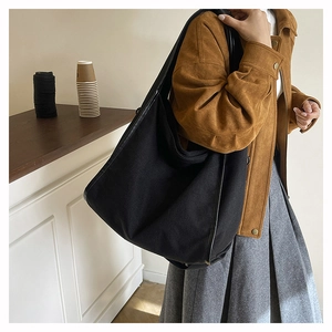 Detail of minimalist black canvas tote bag with leather trim worn over a brown suede jacket