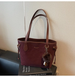 Détail du sac cabas en daim bordeaux avec lettrage doré et breloque pompon en fourrure