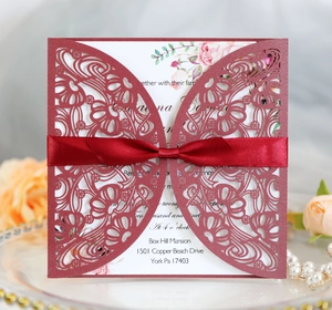 Close-up of laser-cut burgundy wedding card with floral patterns and silk ribbon bow