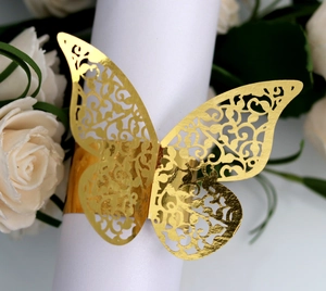Close-up of golden laser-cut butterfly napkin ring on white fabric with floral decor
