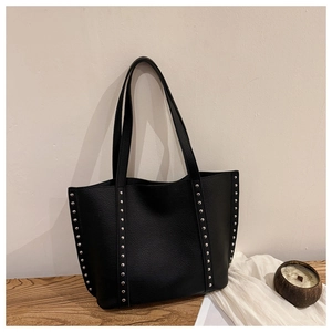 Close-up of black leather tote bag featuring modern silver rivet studs on textured leather