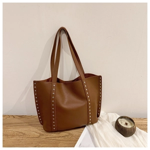 Close-up of brown leather tote bag with silver stud accents on a rustic wood surface