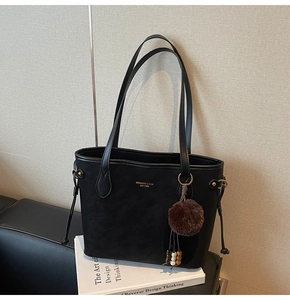 Gros plan du sac cabas noir mat avec logo doré sur livre et accessoire porte-clés en fourrure