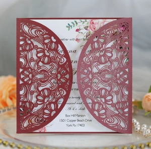 Detail of burgundy laser-cut lace wedding invitation with white floral insert on gold tray