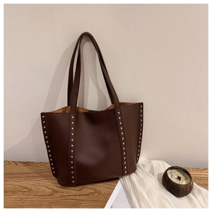 Close-up of vintage brown leather tote bag with silver rivets and grainy texture details