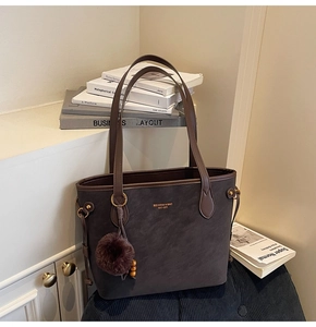 Gros plan sur le sac cabas en daim marron foncé avec pompon en peluche violet et bois