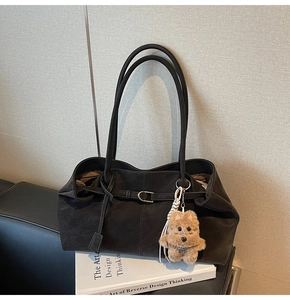 Detail of black suede tote bag with metal buckle and brown plush puppy charm