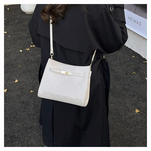 Detail of off-white quilted crossbody bag with gold metal clasp on black coat