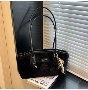 Detail der schwarzen Plüsch-Achseltasche mit Perlenquaste und Metalllogo-Akzent