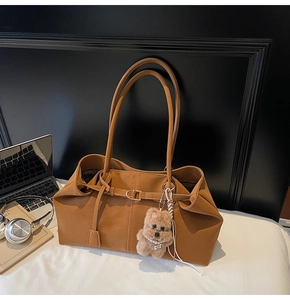 Detail of tan suede tote bag with slim straps and a cute plush bear charm on white desk