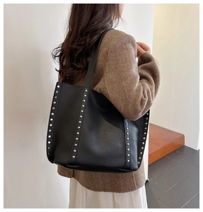 Detail view of black leather tote bag with silver metal studs on the side strap