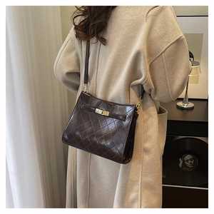 Detail of dark brown quilted leather underarm bag with gold metal twist lock on model