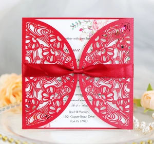 Detailed laser-cut red wedding invitation with elegant silk bow and floral inner page