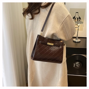 Detail of dark brown quilted shoulder bag with gold metal twist lock on beige coat