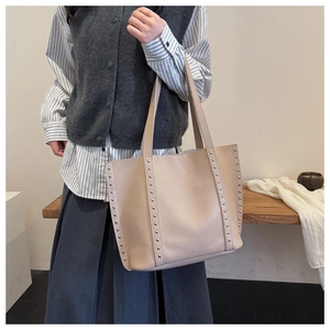 Detail view of beige leather tote bag with silver studs and long handles on a wooden bench