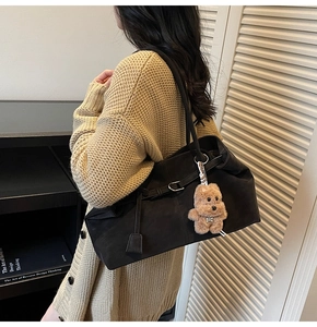 Minimalist black suede tote bag detail with plush teddy bear charm on model's shoulder