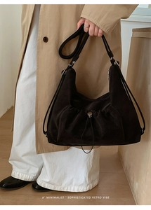 Detail of minimalist black suede crossbody bag with drawstring design and silver buckle