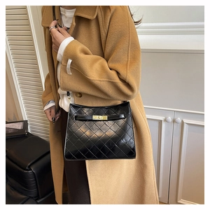 Detail of black quilted shoulder bag featuring glossy finish and gold metal turn-lock